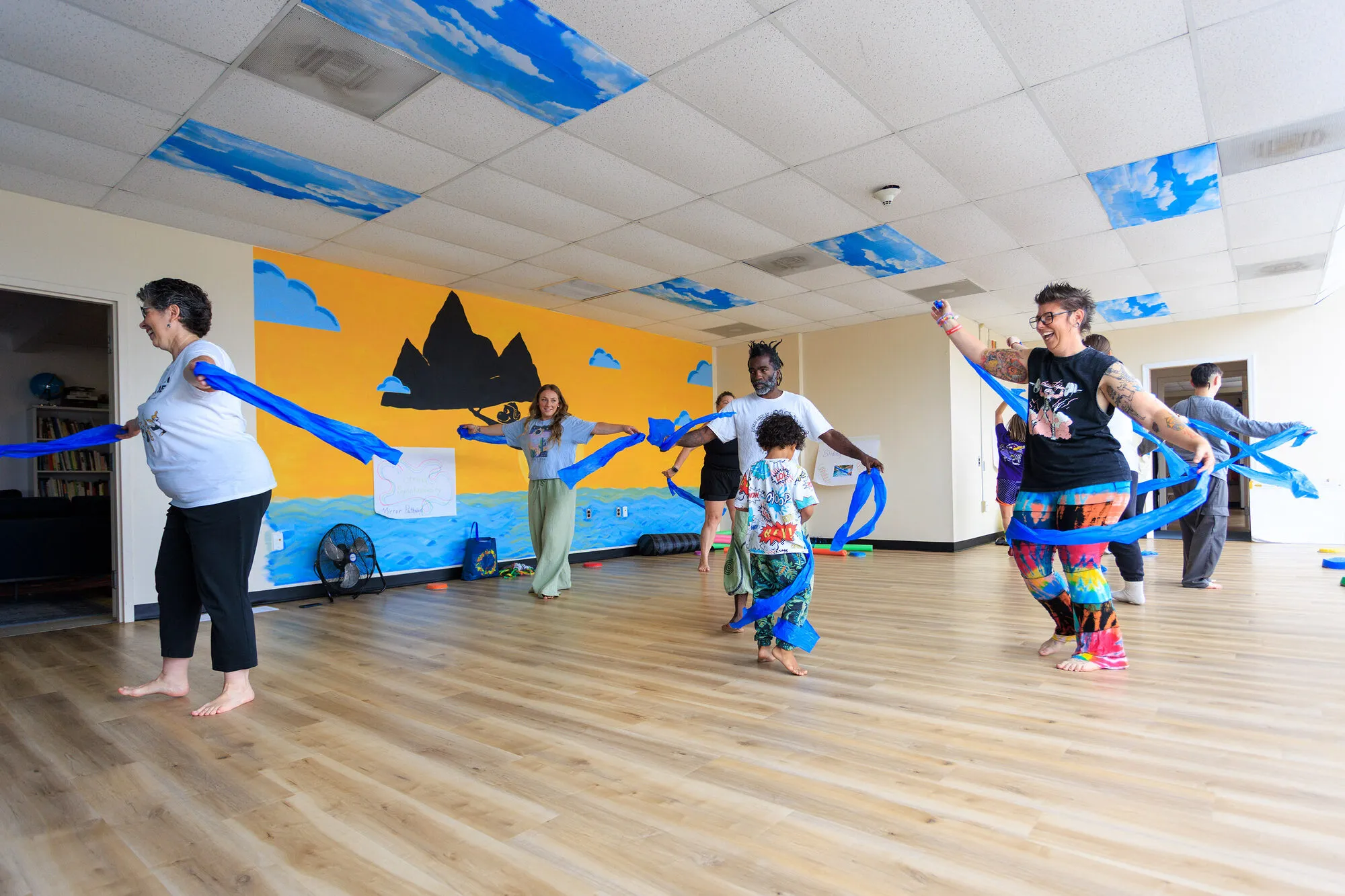 A class at the club moving together with long blue streamers in front of the mountain mural
