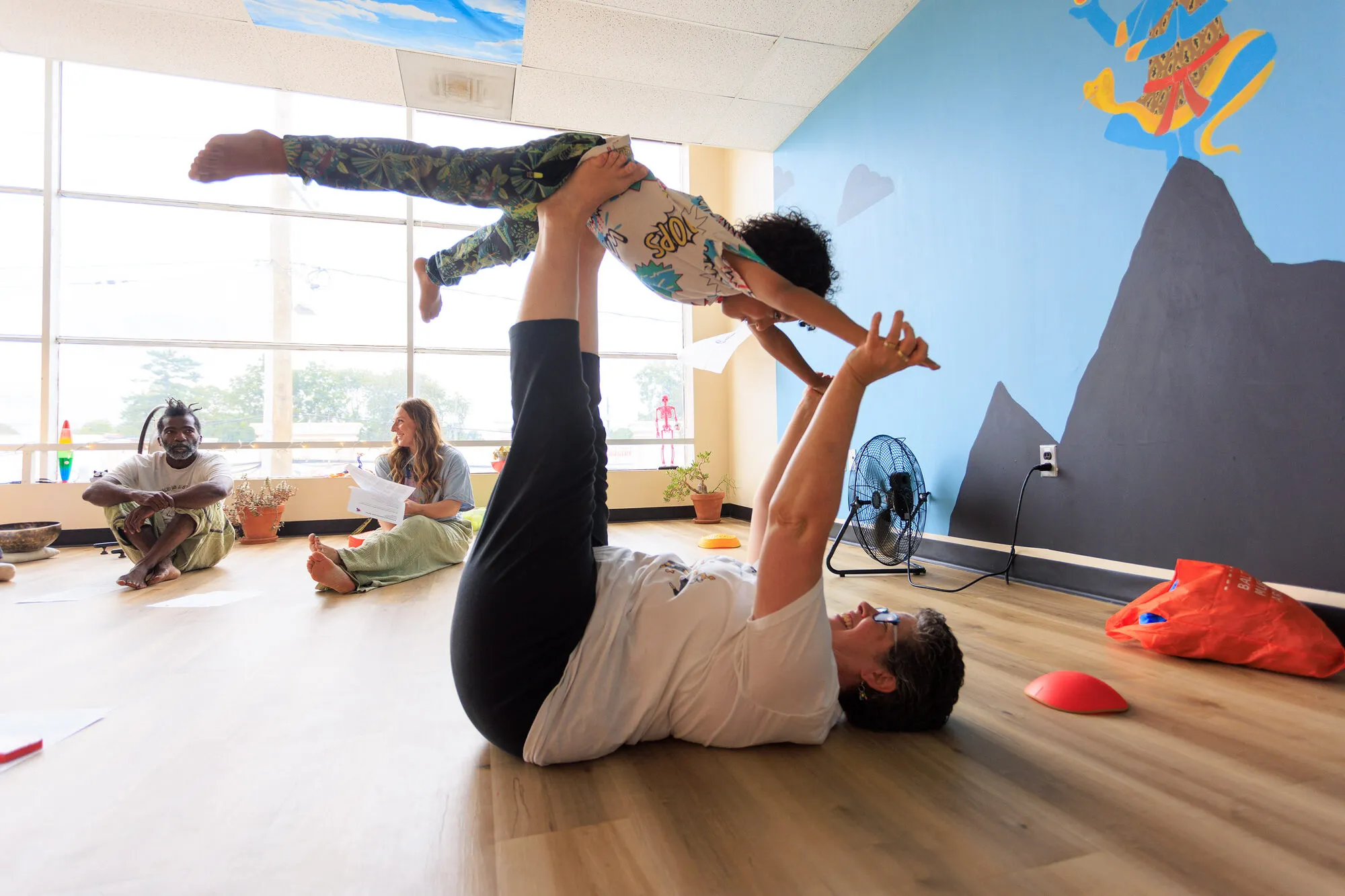 An adult lying on the studio floor balancing a laughing child overhead