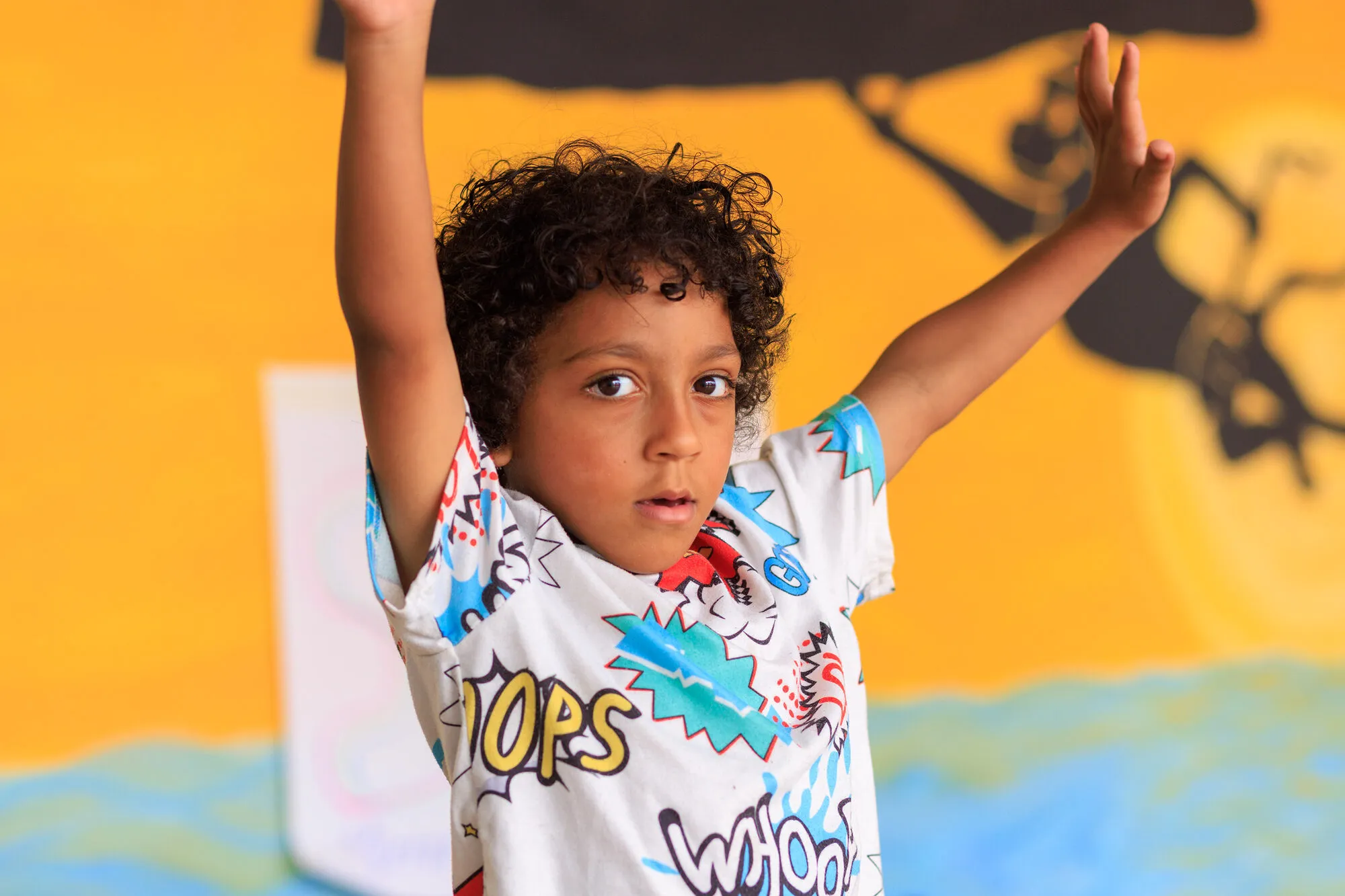 A child with both arms raised in front of the hand-painted mural at the club