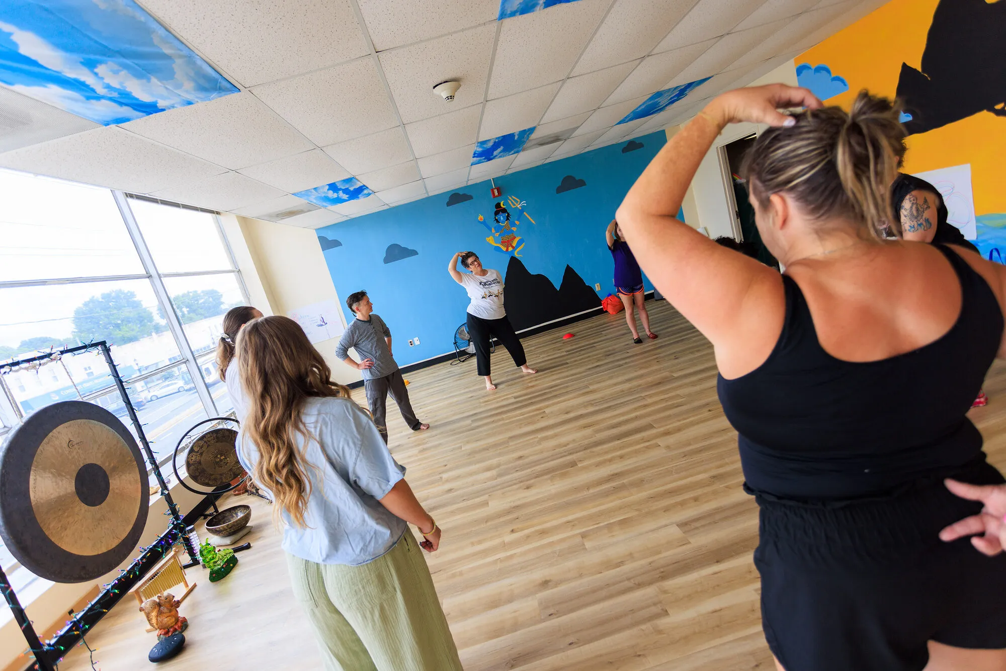 A class in the Sangha House studio, with the gong and the wall of windows behind them